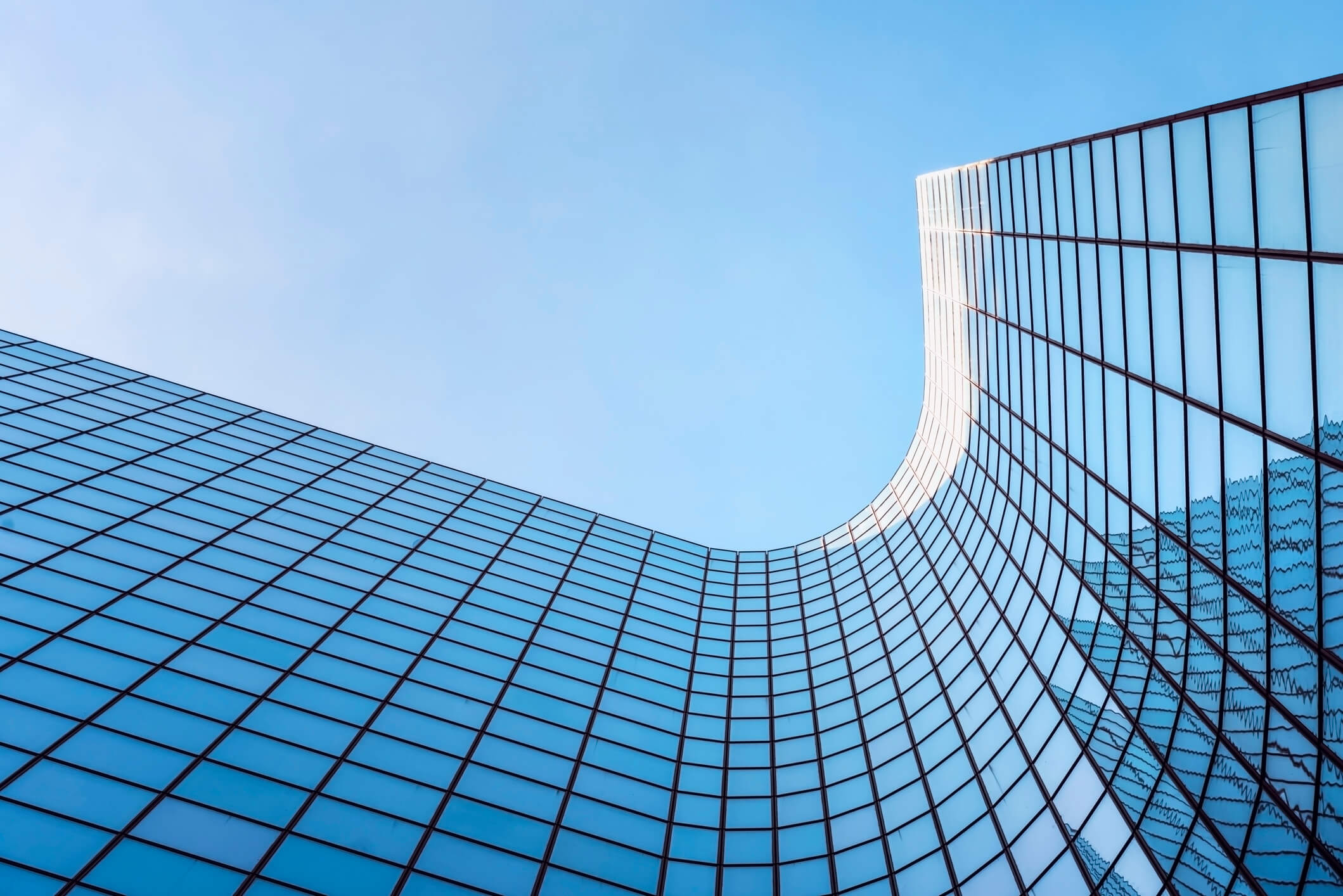 bottom view of a curved building with a glass front reflecting the colour of the sky